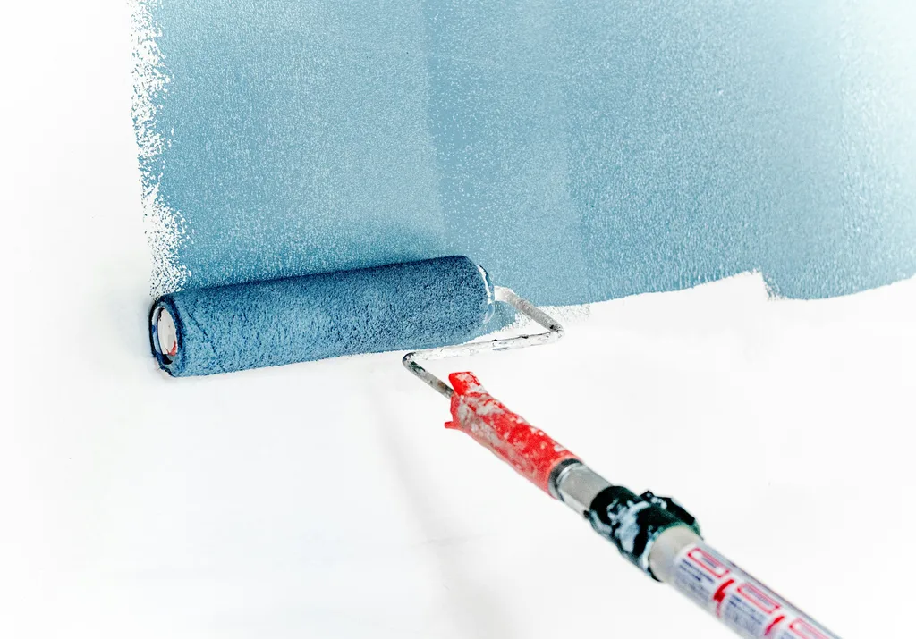 Paint roller spreading soft blue paint across a white interior wall on an extension pole