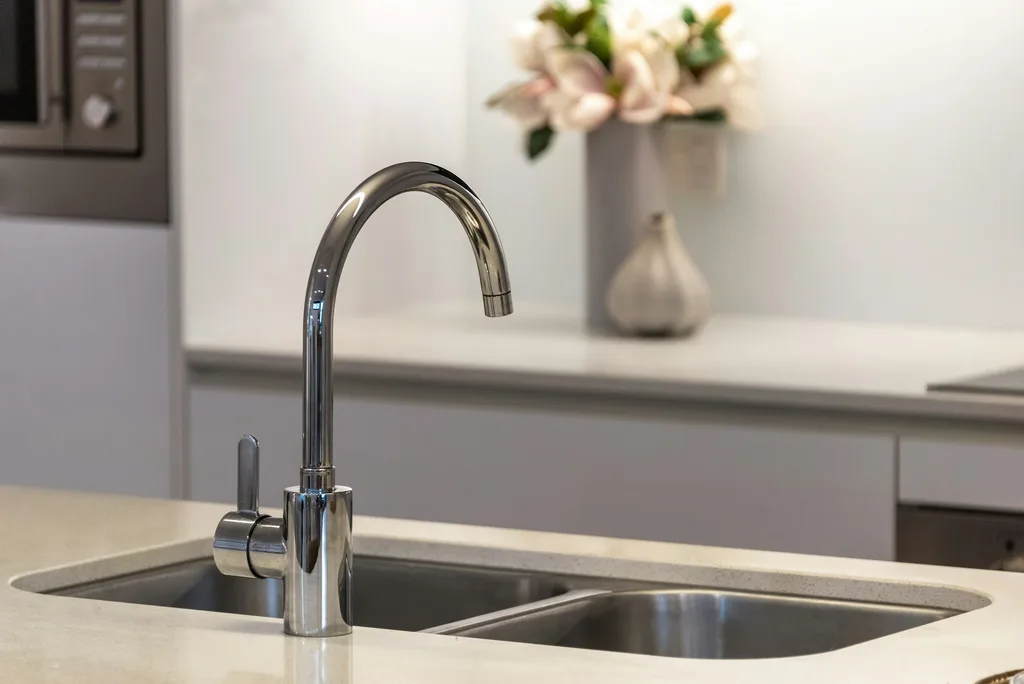Polished chrome gooseneck faucet mounted over a stainless steel kitchen sink and stone countertop